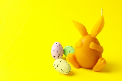 Photo of Beautiful candle and candies on yellow background, closeup with space for text. Easter decor