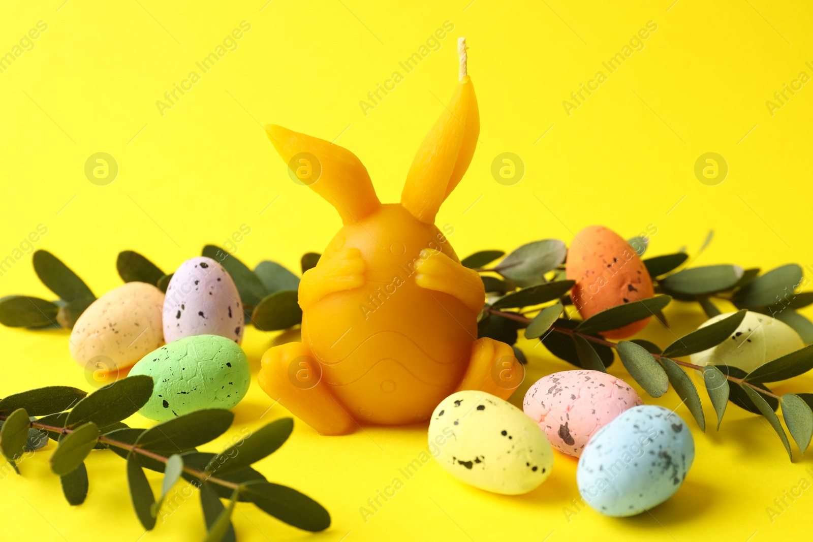 Photo of Beautiful candle, candies and leaves on yellow background, closeup. Easter decor