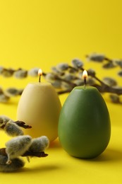 Photo of Beautiful burning egg shaped candles and pussy willow on yellow background, closeup. Easter decor