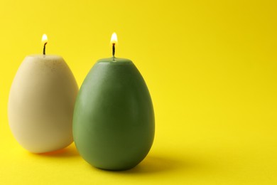 Photo of Beautiful burning egg shaped candles on yellow background, closeup with space for text. Easter decor