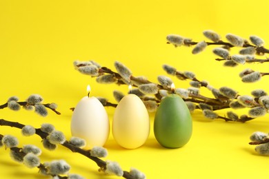 Photo of Beautiful burning egg shaped candles and pussy willow on yellow background. Easter decor