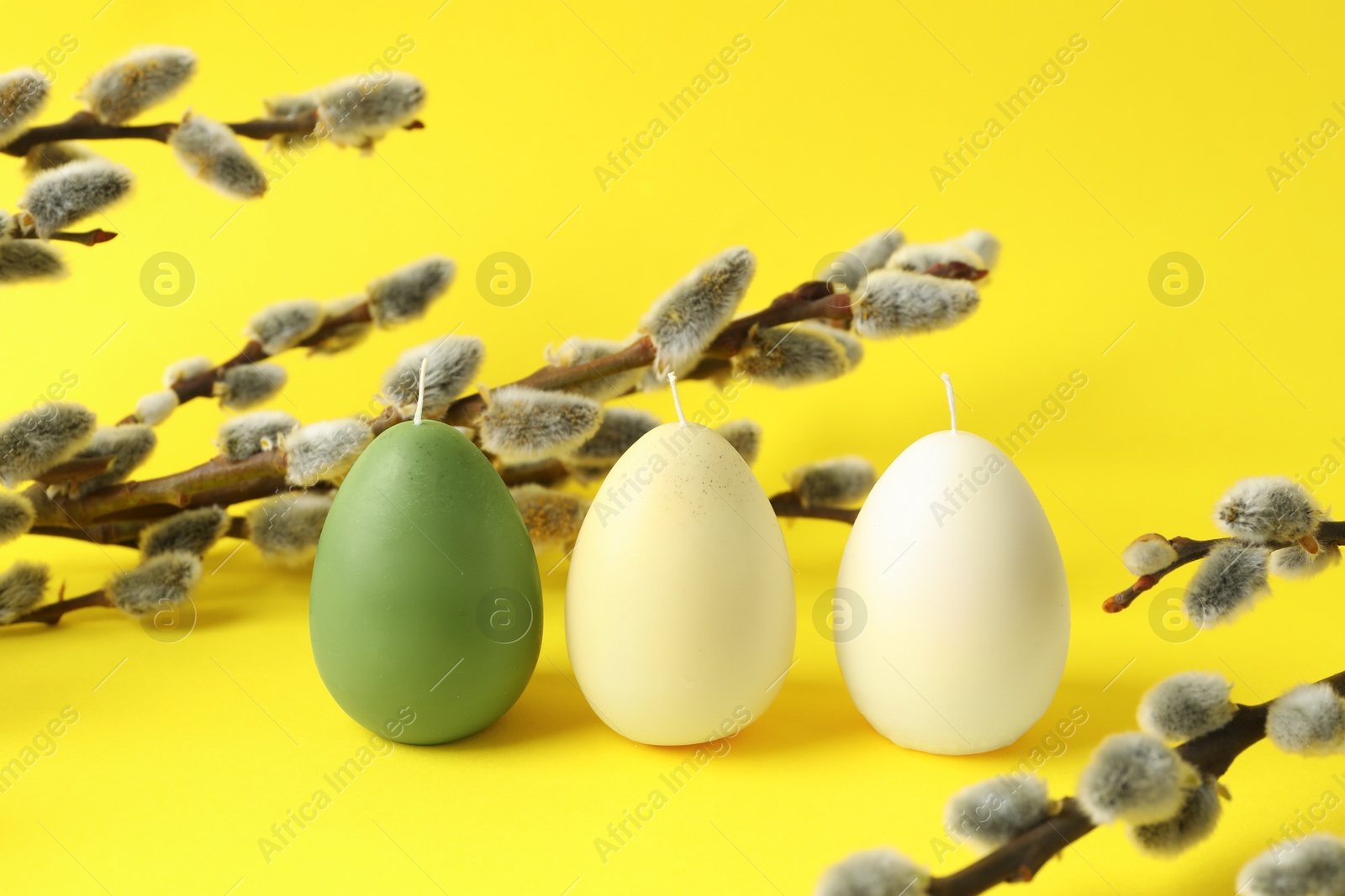 Photo of Beautiful egg shaped candles and pussy willow on yellow background. Easter decor