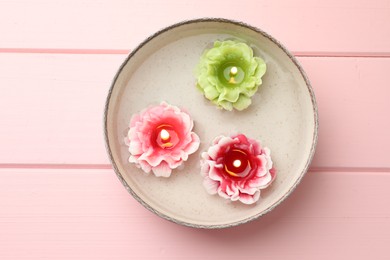 Photo of Beautiful burning flower shaped candles in dish with water on pink wooden table, top view