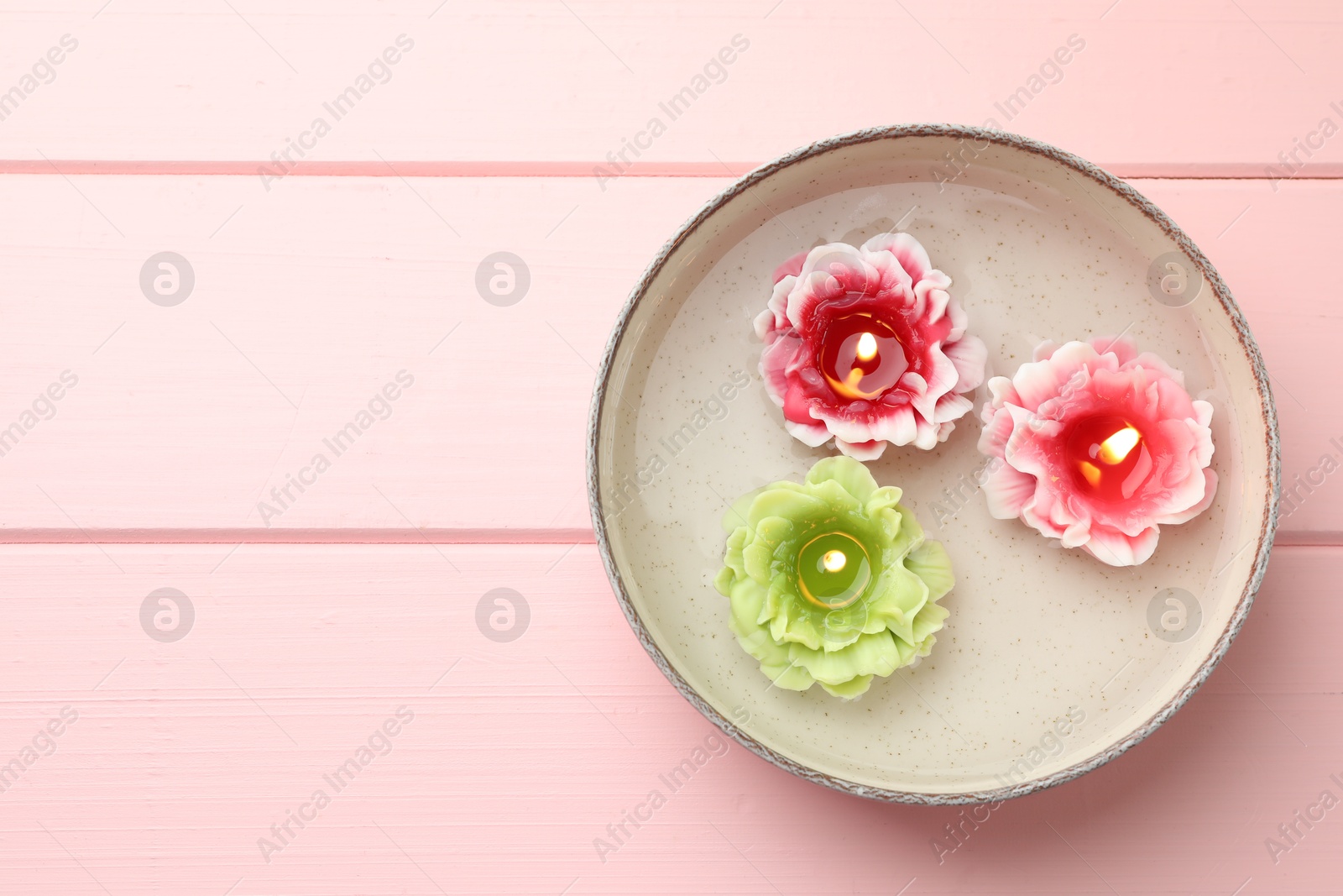 Photo of Beautiful burning flower shaped candles in dish with water on pink wooden table, top view. Space for text