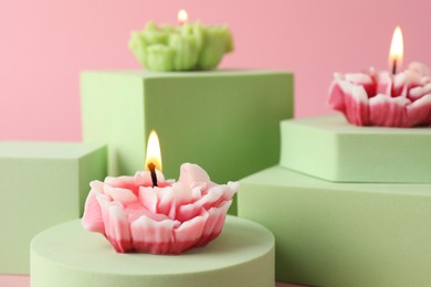 Photo of Beautiful burning flower shaped candles on pink background, closeup