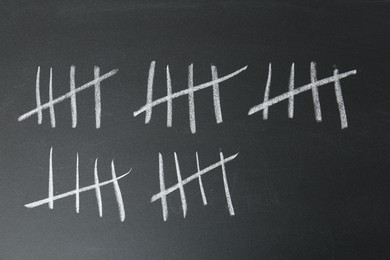 Photo of Counting days by drawing sticks with chalk on blackboard, closeup