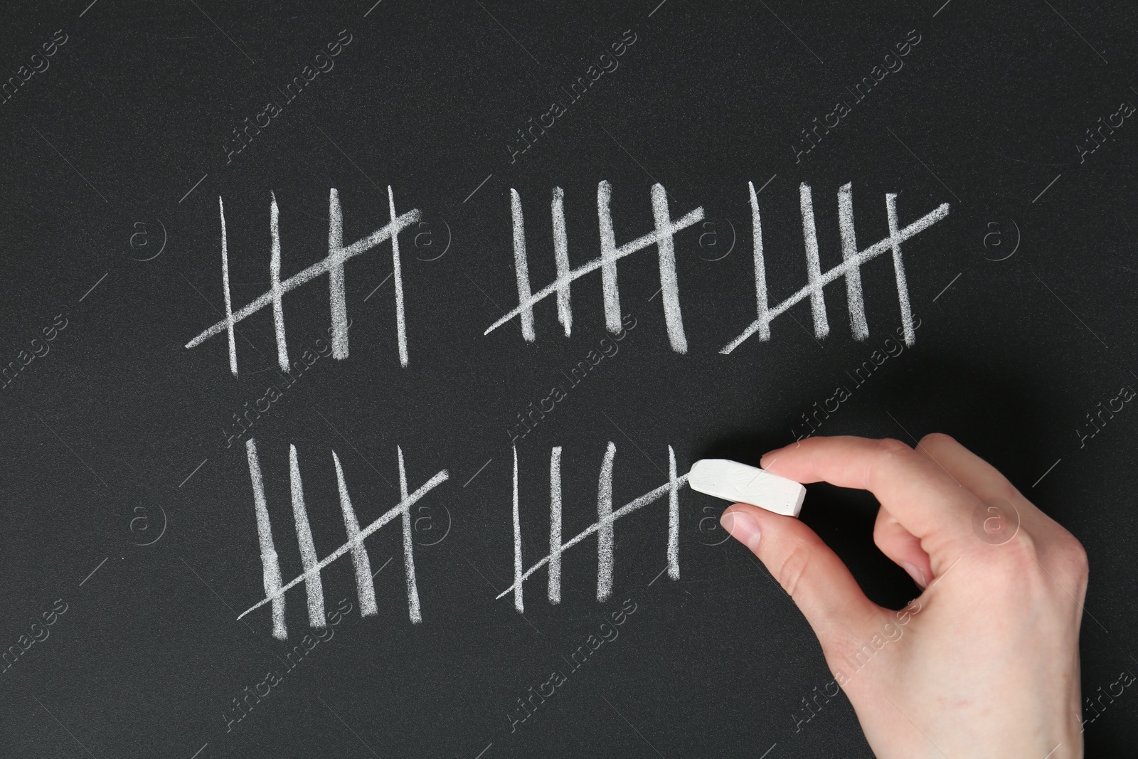 Photo of Woman counting days by drawing sticks with chalk on blackboard, closeup