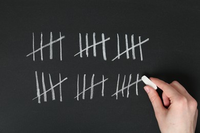 Photo of Woman counting days by drawing sticks with chalk on blackboard, closeup