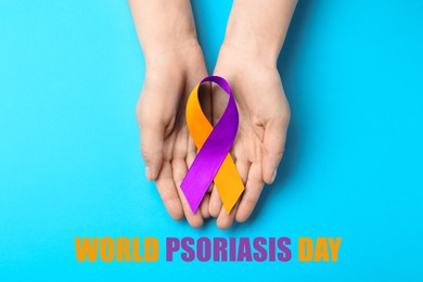 Image of World Psoriasis Day. Woman holding orange-orchid awareness ribbon on light blue background, top view