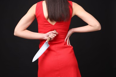 Photo of Businesswoman with knife behind her back on black background, closeup