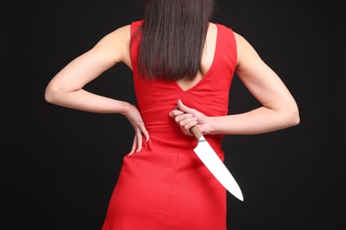 Photo of Businesswoman with knife behind her back on black background, closeup