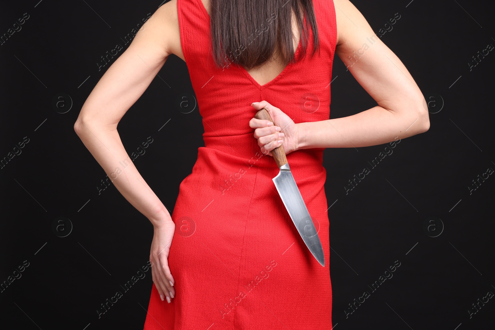 Photo of Businesswoman with knife behind her back on black background, closeup