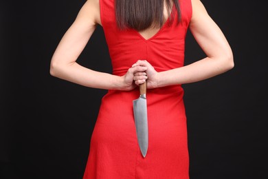 Photo of Businesswoman with knife behind her back on black background, closeup