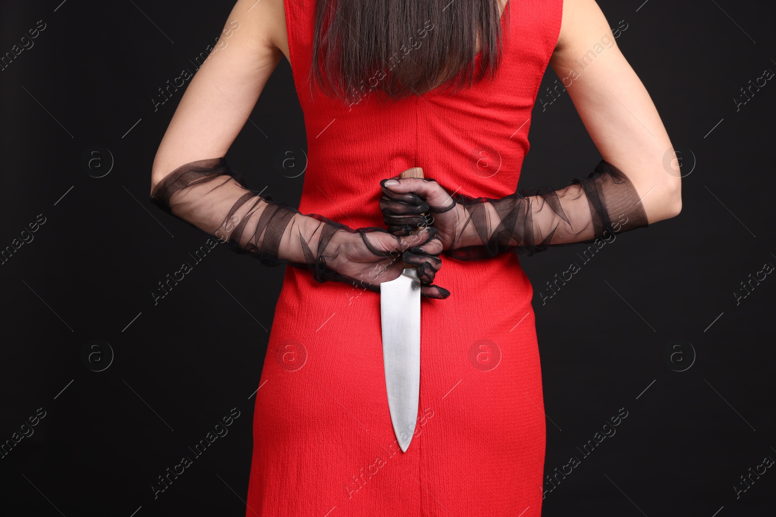 Photo of Businesswoman with knife behind her back on black background, closeup