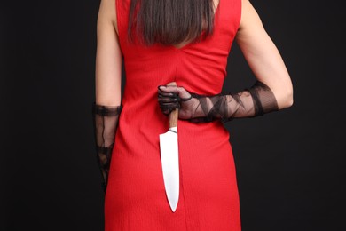 Photo of Businesswoman with knife behind her back on black background, closeup