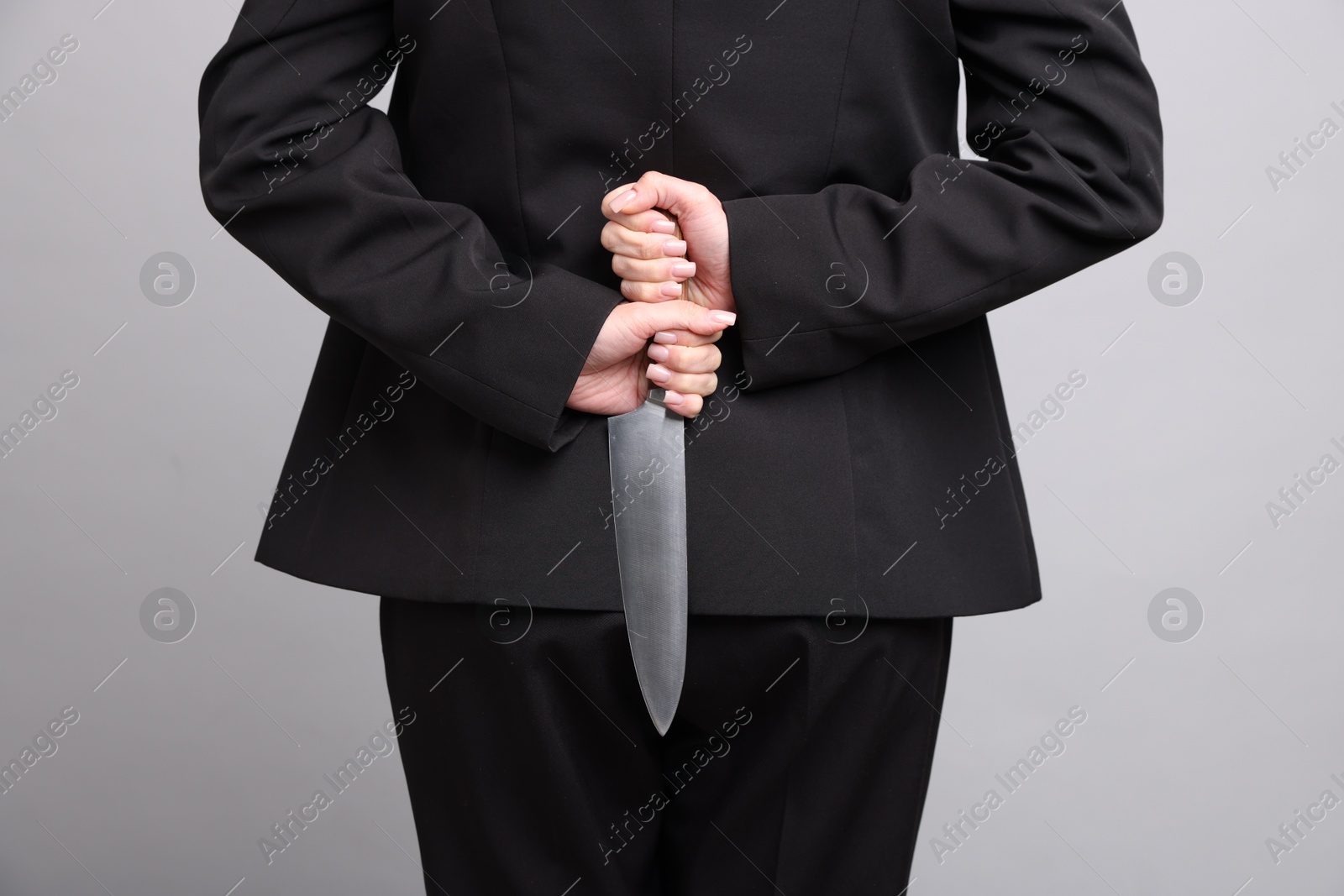 Photo of Businesswoman with knife behind her back on light grey background, closeup