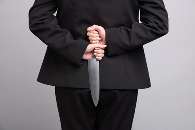 Photo of Businesswoman with knife behind her back on light grey background, closeup