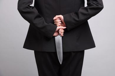 Photo of Businesswoman with knife behind her back on light grey background, closeup