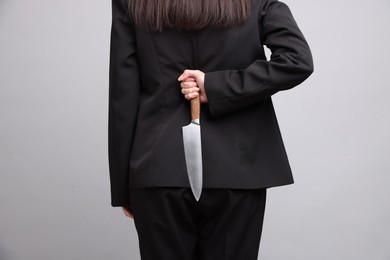 Photo of Businesswoman with knife behind her back on light grey background, closeup