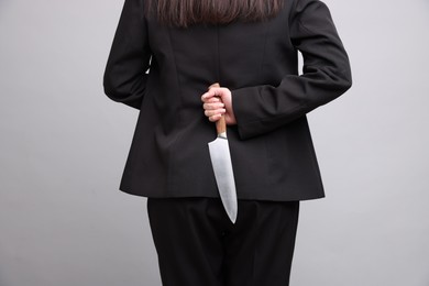 Photo of Businesswoman with knife behind her back on light grey background, closeup