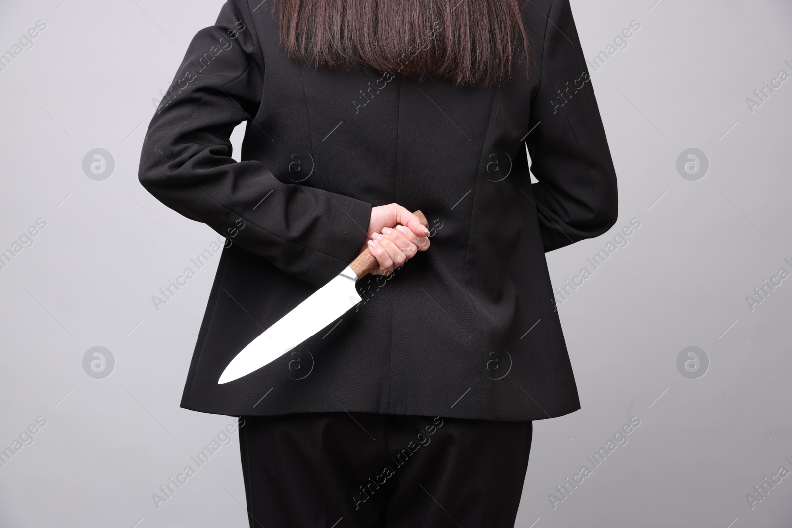 Photo of Businesswoman with knife behind her back on light grey background, closeup