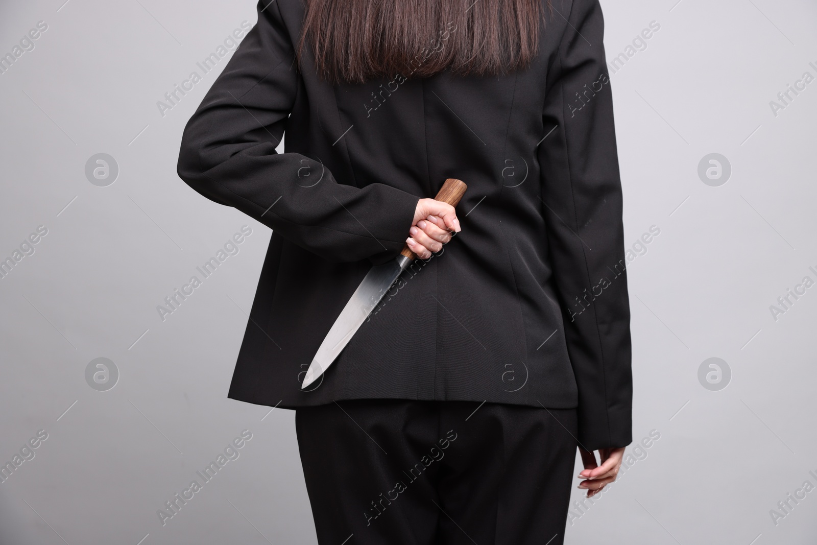 Photo of Businesswoman with knife behind her back on light grey background, closeup