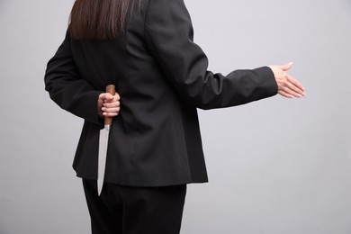 Photo of Businesswoman greeting someone with knife behind her back on light grey background, closeup