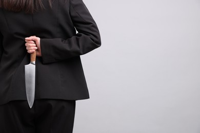 Photo of Businesswoman with knife behind her back on light grey background, closeup. Space for text