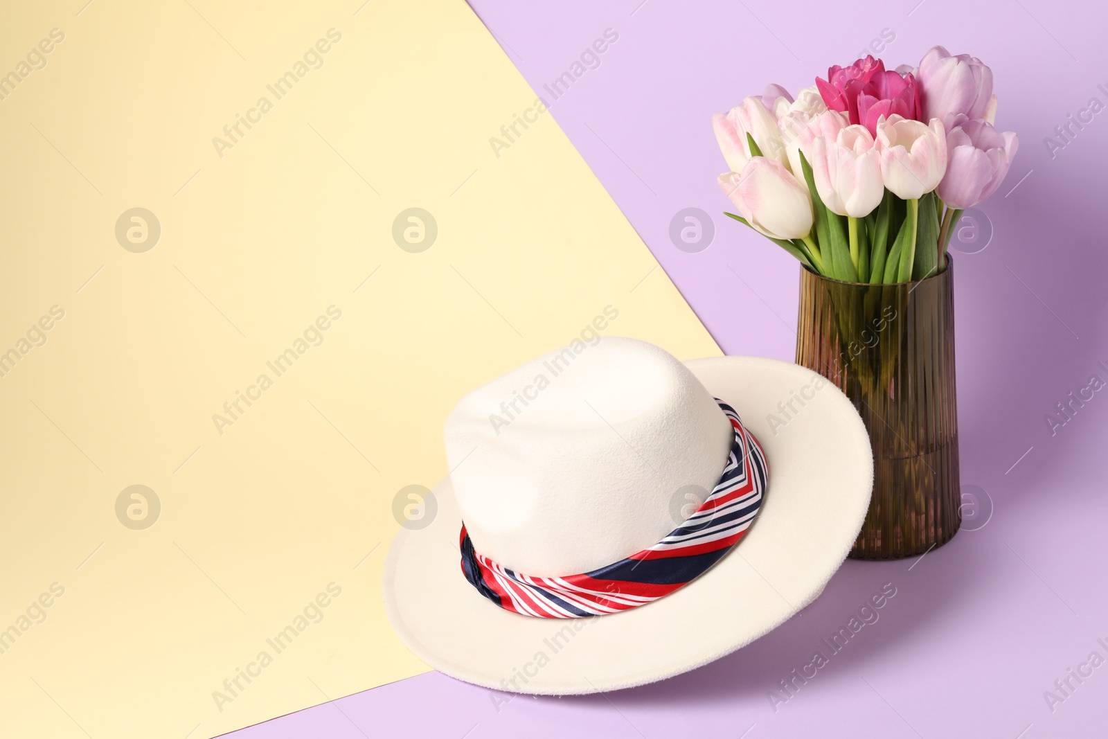 Photo of Hat with striped scarf and tulips on color background. Space for text