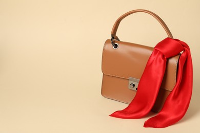 Photo of Handbag with red scarf on beige background. Space for text