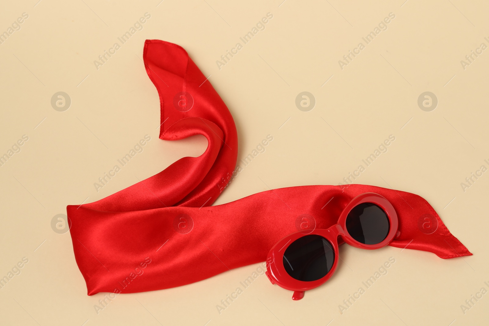 Photo of Beautiful red neck scarf and sunglasses on beige background, top view