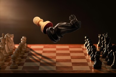 Image of Chess game. Black knight beating white pawn in air over chessboard