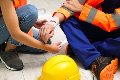 Photo of Accident at work. Woman putting bandage on her colleague's injured wrist in warehouse, closeup