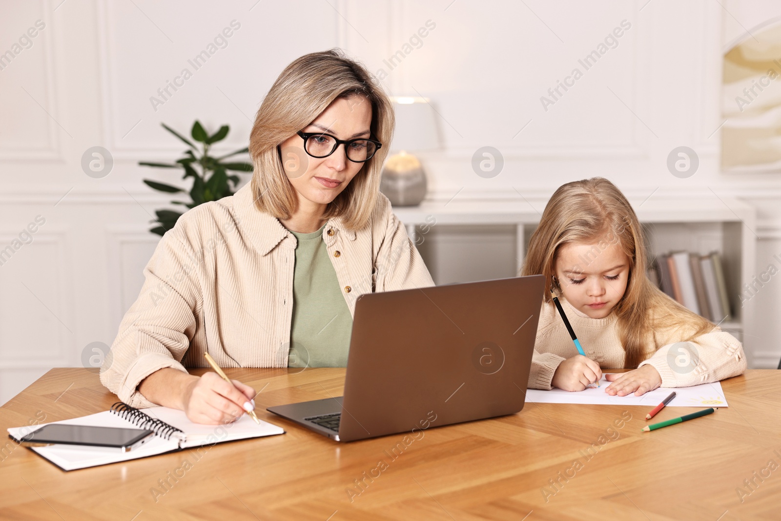 Photo of Single mother working and her daughter drawing at wooden table indoors