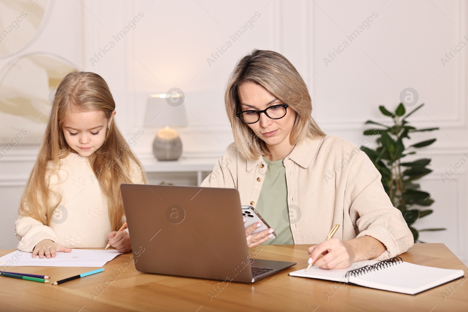 Photo of Single mother working and her daughter drawing at wooden table indoors