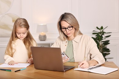 Photo of Single mother working and her daughter drawing at wooden table indoors