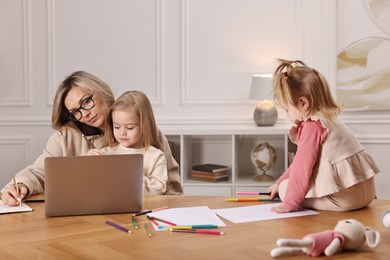 Photo of Work-family balance. Single mother talking by smartphone and her children drawing at wooden table indoors