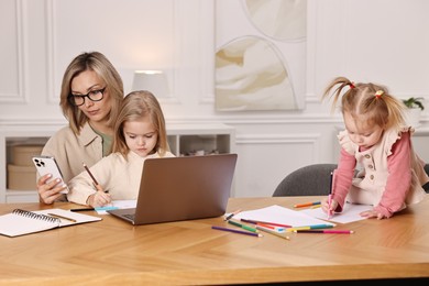 Photo of Single mother working and her children drawing at wooden table indoors