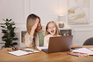 Photo of Work-family balance. Single mother and her naughty screaming daughter at wooden table indoors