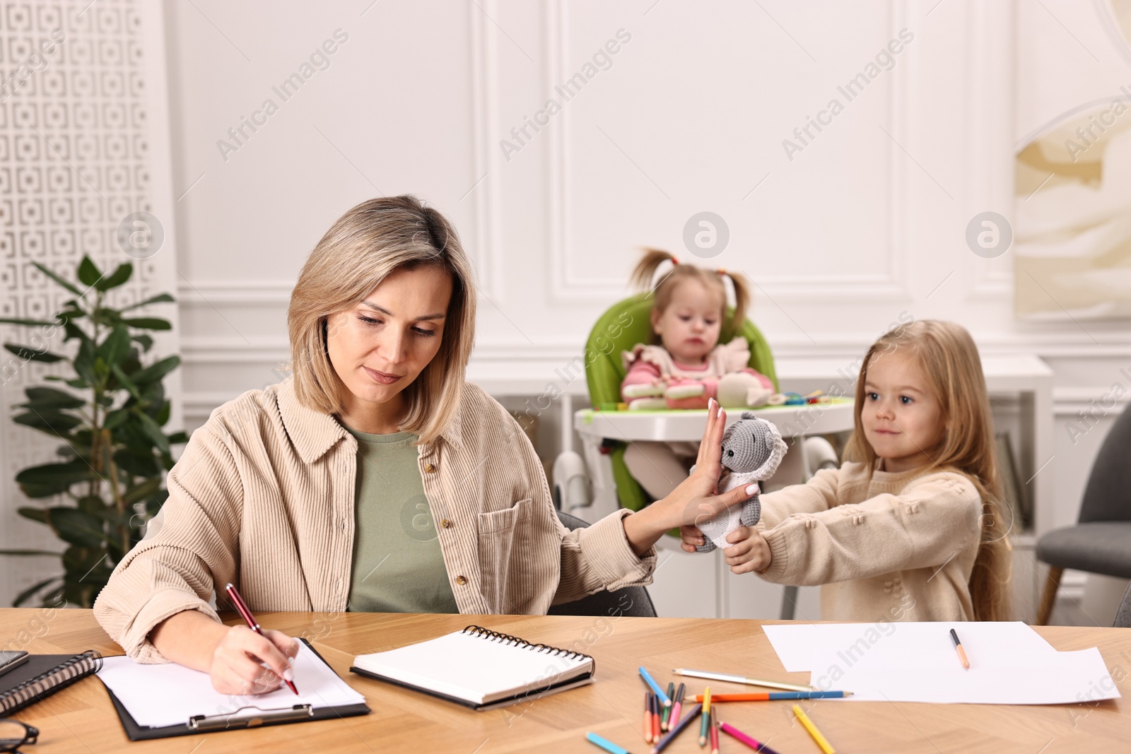 Photo of Single mother working and refusing to play with her daughter at wooden table indoors