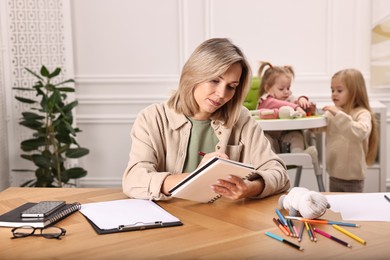 Photo of Single mother working at table while her children playing indoors, selective focus