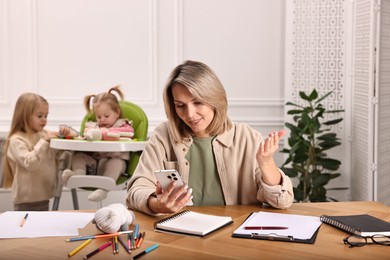 Photo of Work at home. Smiling single mother having videochat by smartphone while her children playing indoors, selective focus