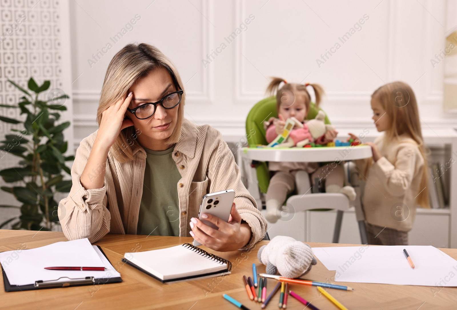 Photo of Work at home. Single mother having videochat by smartphone while her children playing indoors, selective focus