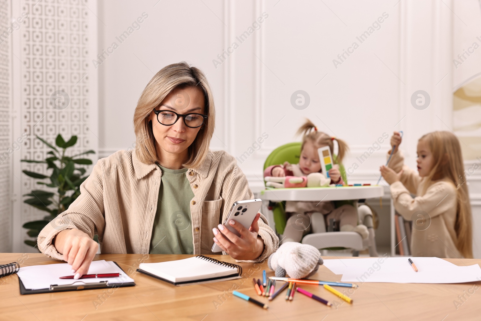 Photo of Single mother working at table while her children playing indoors, selective focus