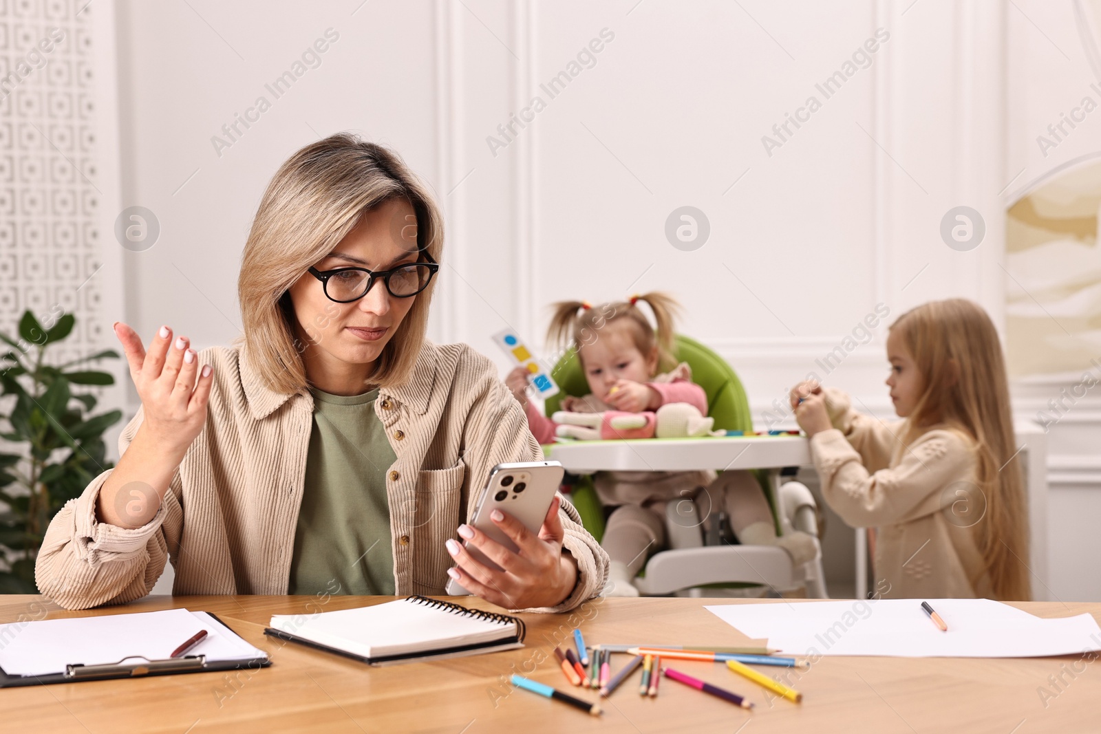 Photo of Work at home. Single mother having videochat by smartphone while her children playing indoors, selective focus