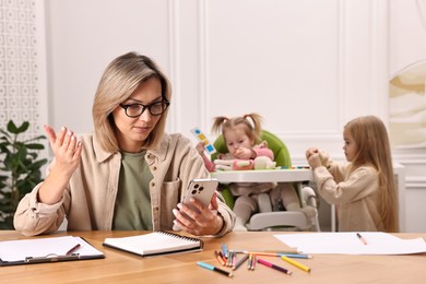 Photo of Work at home. Single mother having videochat by smartphone while her children playing indoors, selective focus