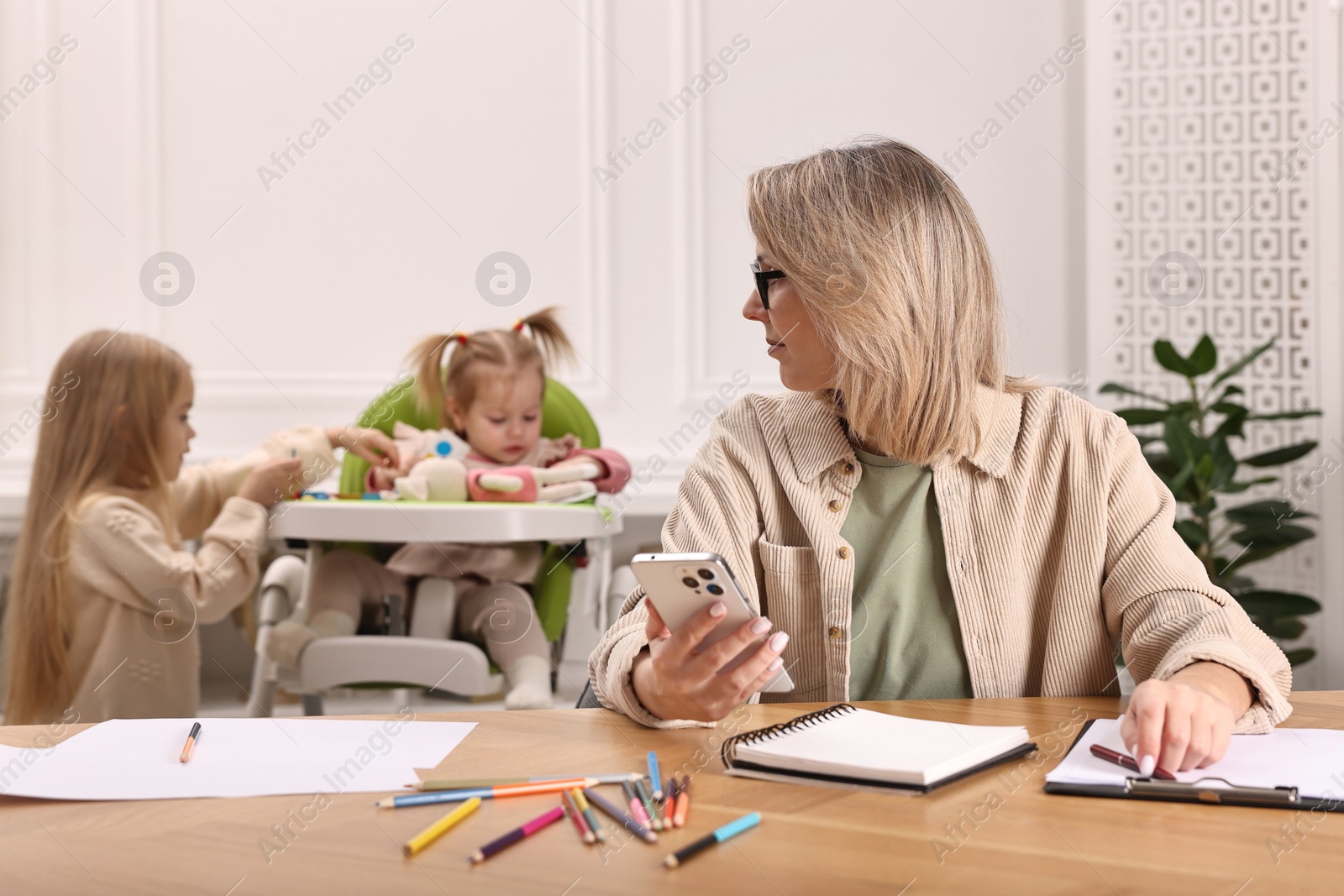 Photo of Single mother working at table while her children playing indoors, selective focus