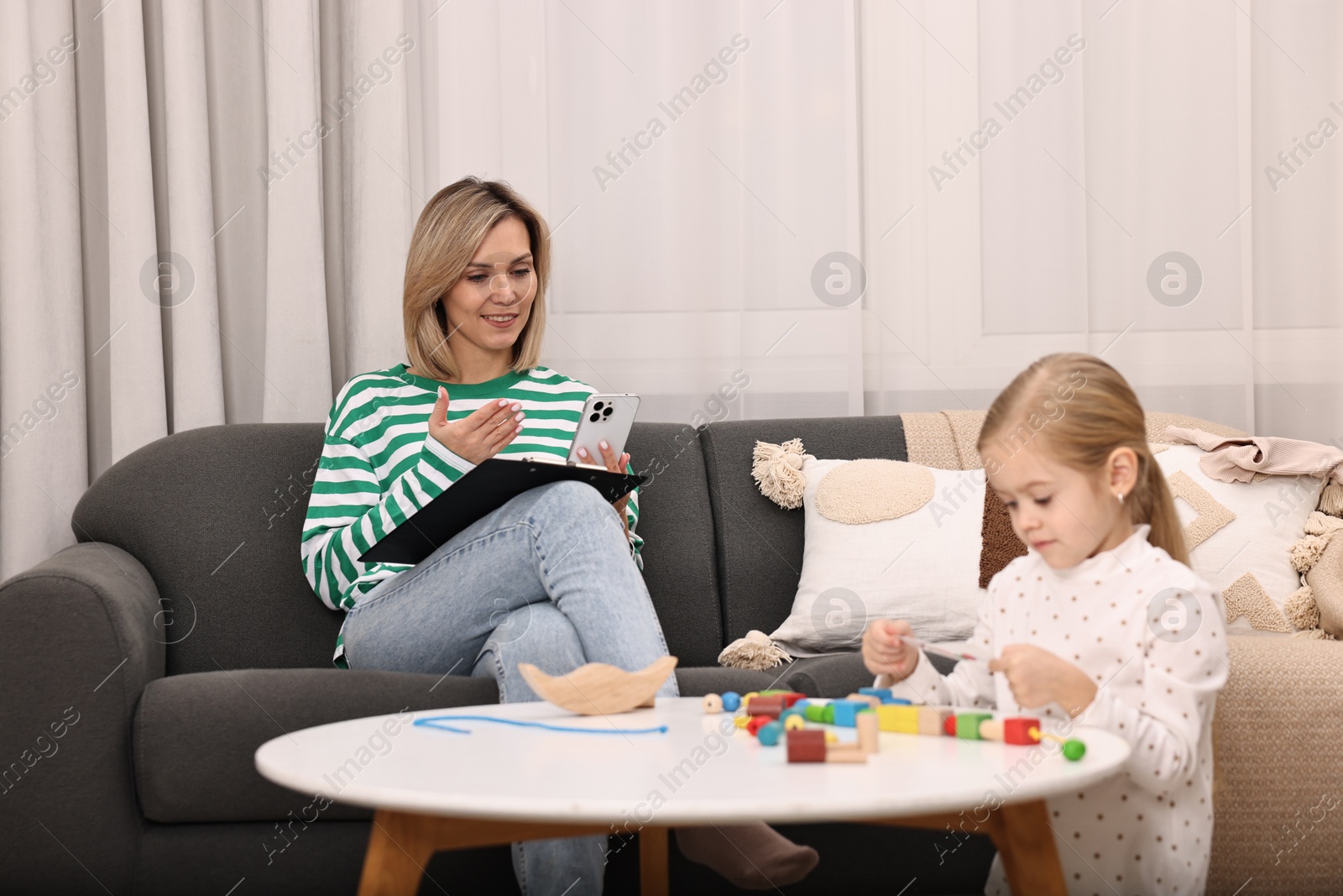 Photo of Work at home. Smiling single mother having videochat by smartphone while her daughter playing indoors