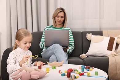 Photo of Single mother working with laptop while her daughter playing at home