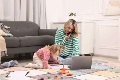 Photo of Work at home. Single mother talking by smartphone and her daughter drawing on floor indoors